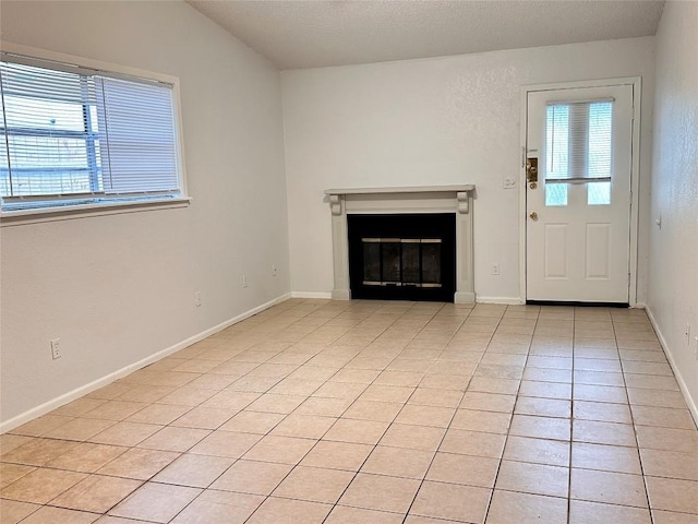 unfurnished living room featuring light tile patterned flooring, baseboards, and a glass covered fireplace