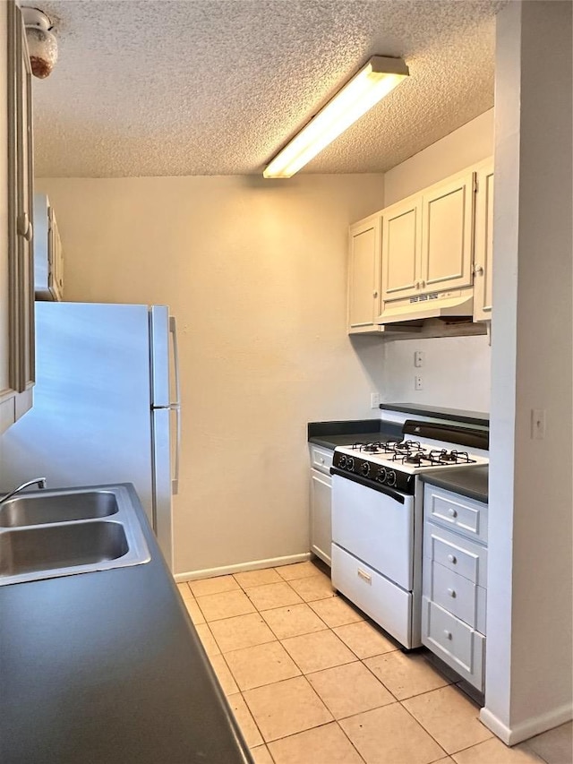 kitchen with white appliances, a textured ceiling, under cabinet range hood, a sink, and light tile patterned floors