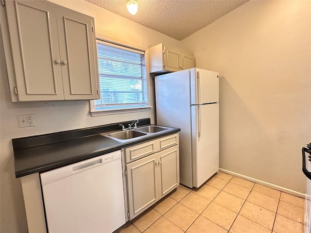 kitchen with light tile patterned flooring, dark countertops, a sink, white appliances, and a textured ceiling