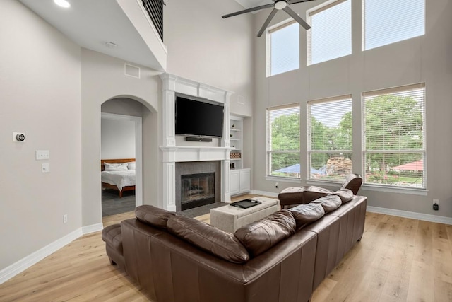 living room featuring light wood-style floors, a ceiling fan, arched walkways, and a high ceiling