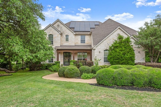 view of front facade featuring a shingled roof, a front yard, stone siding, and solar panels
