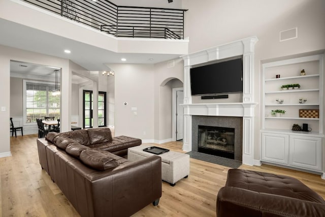 living room featuring light wood-style floors, arched walkways, a fireplace with flush hearth, and a towering ceiling