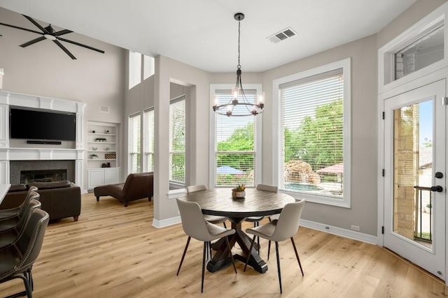 dining room with a glass covered fireplace, baseboards, light wood finished floors, and visible vents