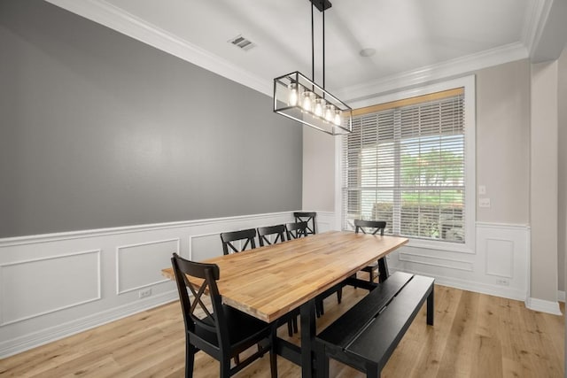 dining room featuring visible vents, ornamental molding, light wood finished floors, and a wainscoted wall