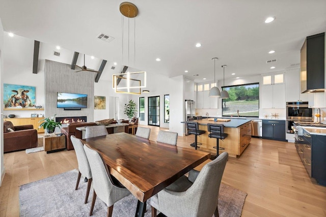 dining space featuring high vaulted ceiling, light wood-style flooring, and visible vents