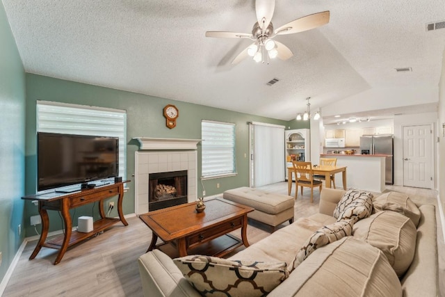 living room featuring visible vents, ceiling fan, a textured ceiling, light wood-style flooring, and vaulted ceiling