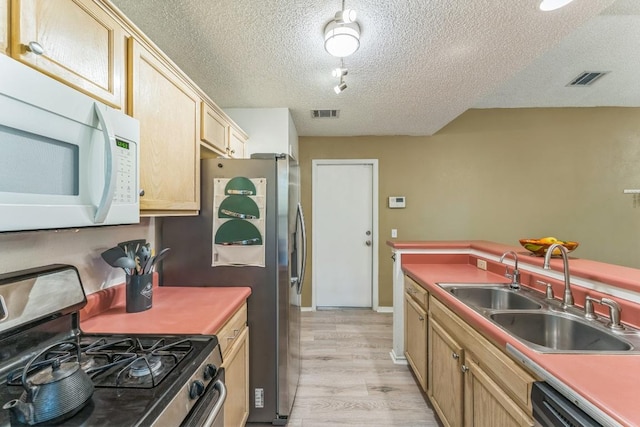 kitchen featuring appliances with stainless steel finishes, a sink, a textured ceiling, light wood-type flooring, and visible vents