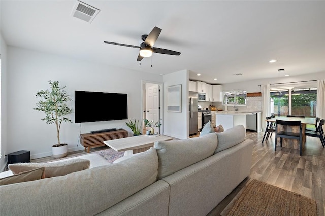 living room featuring ceiling fan, visible vents, wood finished floors, baseboards, and recessed lighting