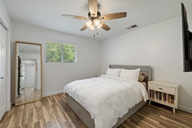 bedroom with baseboards, a ceiling fan, wood finished floors, and visible vents