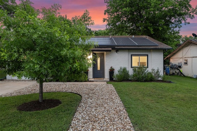 view of front facade with roof mounted solar panels, brick siding, and a front yard