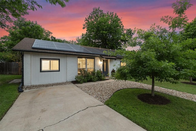 ranch-style house with a lawn, brick siding, fence, and roof mounted solar panels