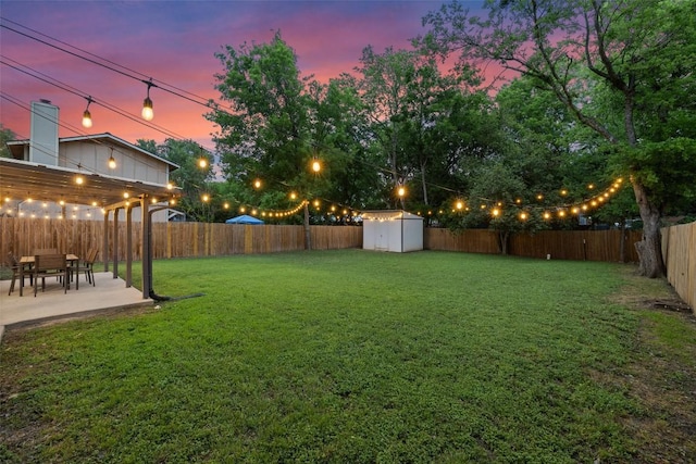 yard at dusk with a fenced backyard, a patio area, a storage shed, and an outbuilding