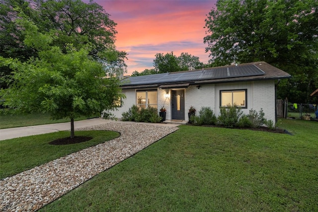 ranch-style home with driveway, a front yard, brick siding, fence, and roof mounted solar panels