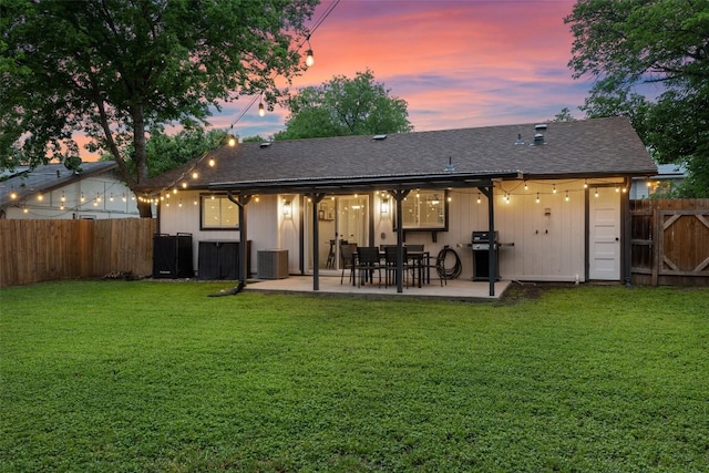 rear view of property with a fenced backyard, a lawn, a patio area, and roof with shingles