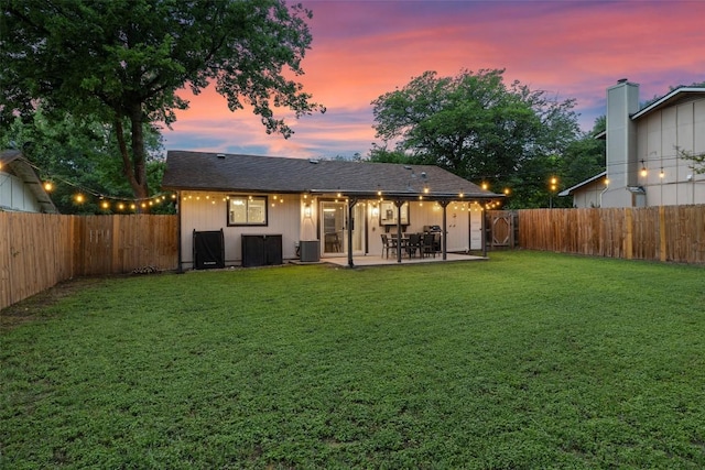 back of property at dusk with a lawn, a fenced backyard, cooling unit, and a patio