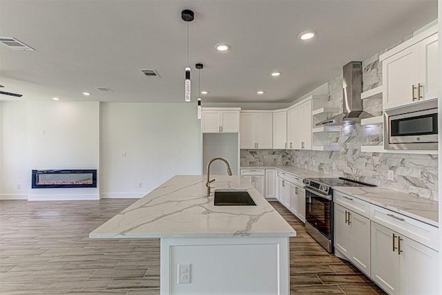 141 Awehi Ln, Bastrop, TX 78602 - kitchen featuring stainless steel appliances, a sink, wall chimney exhaust hood, light wood-style flooring, and a glass covered fireplace