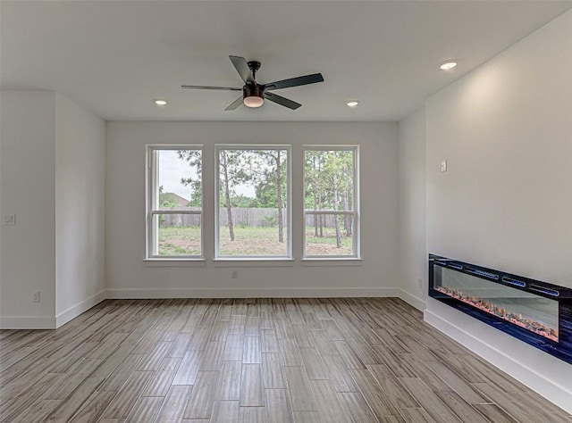 141 Awehi Ln, Bastrop, TX 78602 - unfurnished room with a glass covered fireplace, wood finished floors, baseboards, a ceiling fan, and recessed lighting