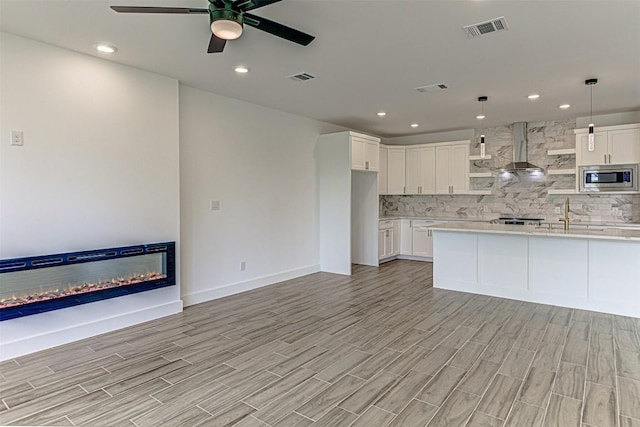 141 Awehi Ln, Bastrop, TX 78602 - kitchen featuring wall chimney range hood, stainless steel microwave, a glass covered fireplace, light countertops, and recessed lighting