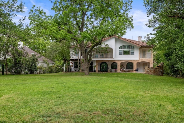 exterior space featuring stucco siding, a chimney, a balcony, and a front lawn