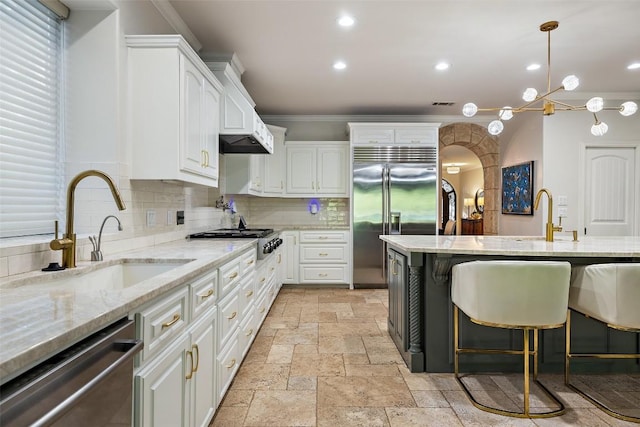 kitchen featuring crown molding, white cabinets, appliances with stainless steel finishes, a sink, and stone tile floors