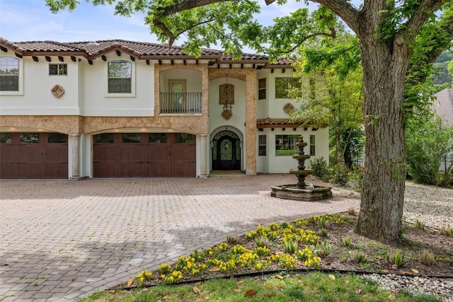 mediterranean / spanish-style home with an attached garage, stucco siding, decorative driveway, and a tile roof