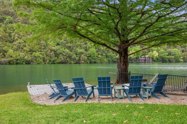 dock area with a water view, a view of trees, fence, and a yard