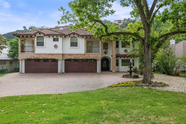 mediterranean / spanish house featuring a tiled roof, a front yard, a garage, decorative driveway, and stucco siding