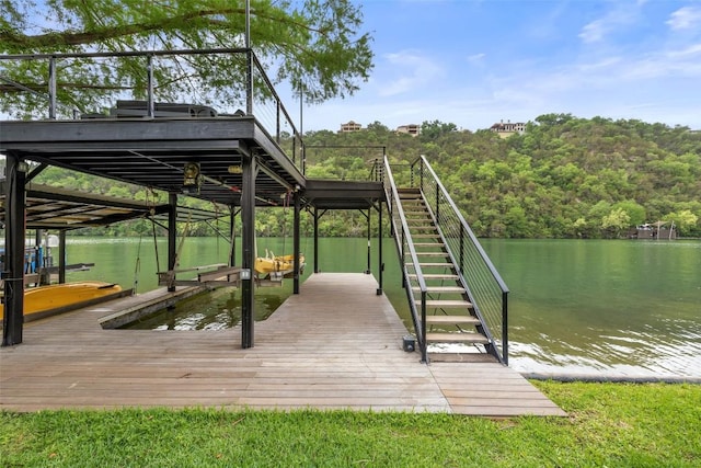 dock area with a wooded view, a water view, boat lift, and stairway