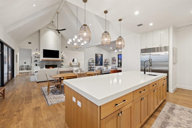 kitchen featuring light wood-style floors, a kitchen island with sink, a large fireplace, open floor plan, and visible vents