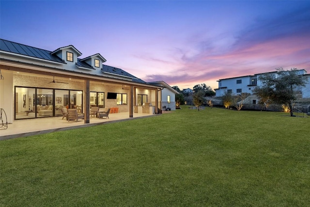 rear view of property with ceiling fan, a patio, an outdoor hangout area, a standing seam roof, and a lawn