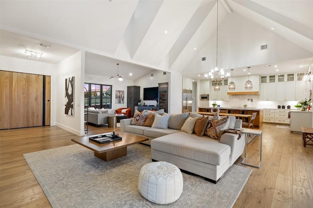 living area featuring high vaulted ceiling, a notable chandelier, visible vents, and light wood-type flooring