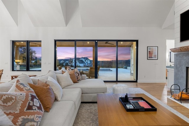 living room featuring baseboards, high vaulted ceiling, wood finished floors, and a fireplace