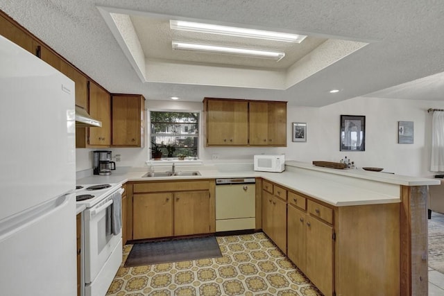 kitchen with a sink, a peninsula, under cabinet range hood, a tray ceiling, and white appliances