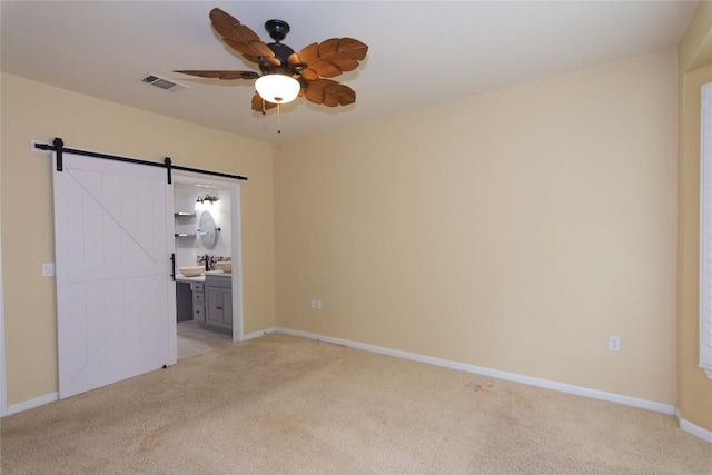 unfurnished bedroom with light colored carpet, baseboards, visible vents, and a barn door