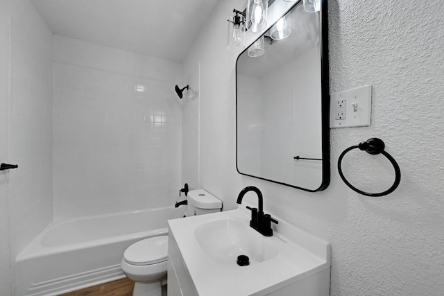 bathroom featuring vanity, a textured wall, wood finished floors, toilet, and shower / bathing tub combination