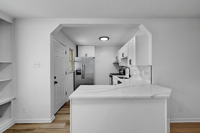 kitchen with light stone counters, a peninsula, light wood-style floors, and appliances with stainless steel finishes