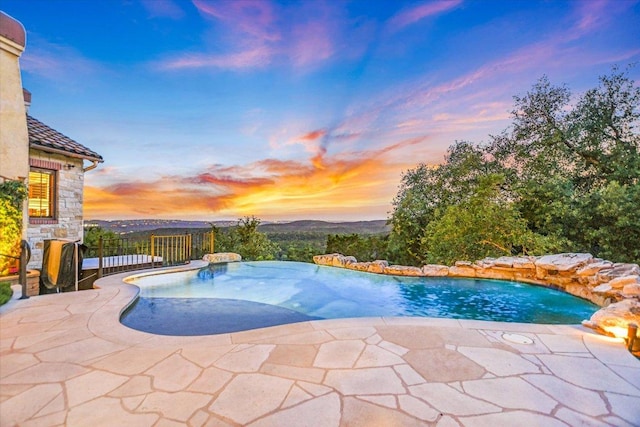 pool at dusk with an infinity pool, a patio, and fence