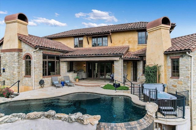 back of house with a tiled roof, a chimney, a patio area, and stone siding