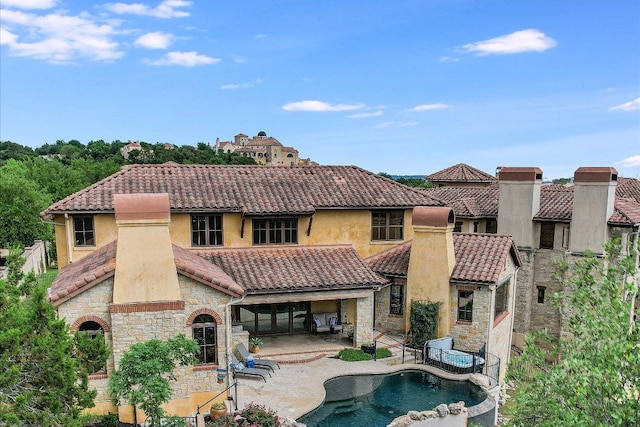 back of property featuring a patio area, a pool with connected hot tub, a tiled roof, and stone siding