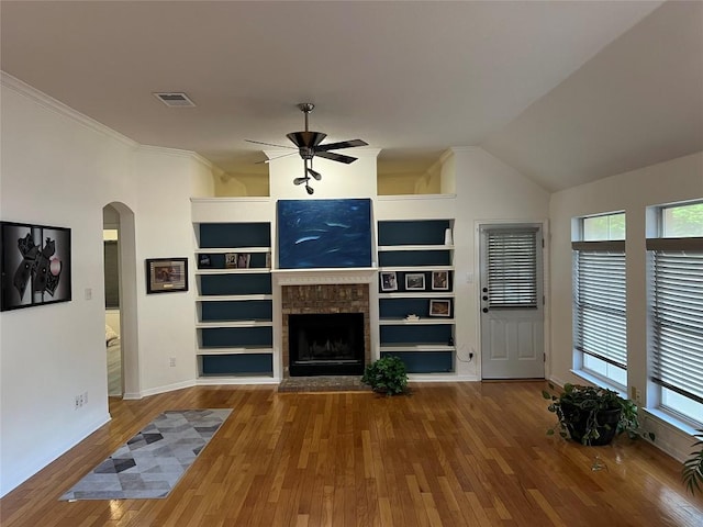 unfurnished living room featuring arched walkways, a ceiling fan, a wealth of natural light, wood finished floors, and visible vents
