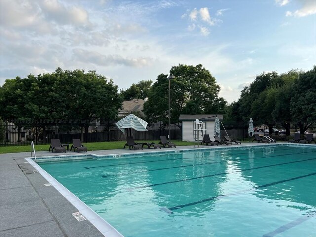 community pool featuring a storage unit, an outdoor structure, a lawn, and fence