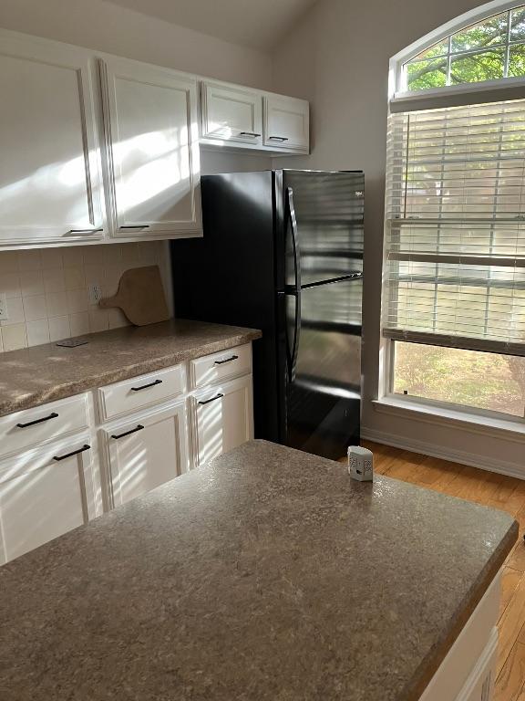 1728 Dapplegrey Ln, Austin, TX 78727 - kitchen with white cabinetry, wood finished floors, freestanding refrigerator, decorative backsplash, and dark stone countertops