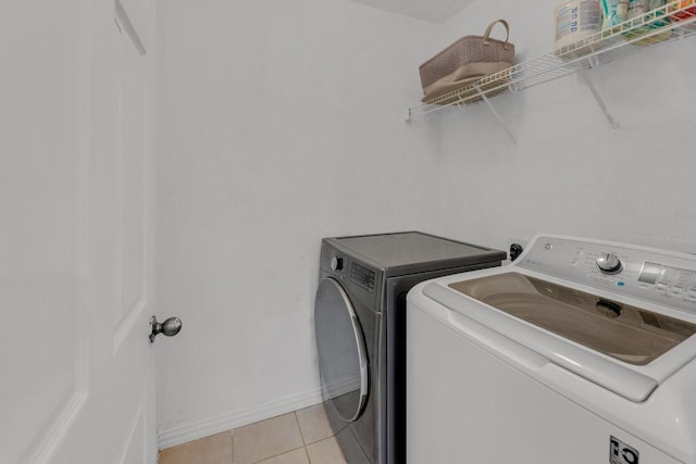 clothes washing area with light tile patterned floors, baseboards, laundry area, and washer and clothes dryer