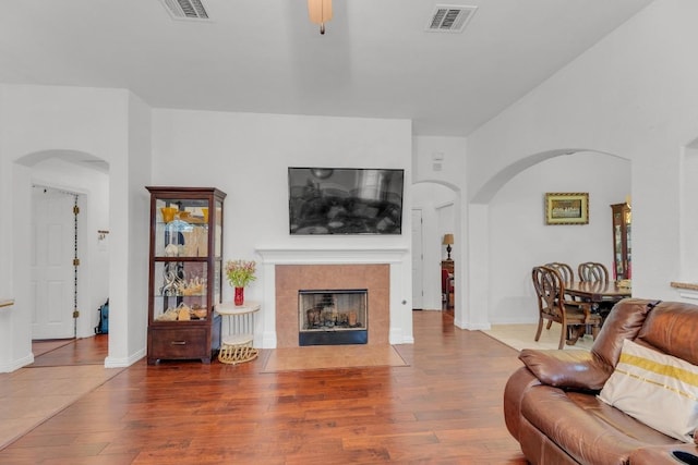 living area with visible vents, arched walkways, wood finished floors, and a tile fireplace