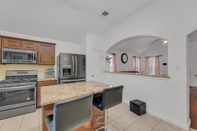 kitchen with a center island, tasteful backsplash, arched walkways, appliances with stainless steel finishes, and vaulted ceiling