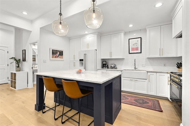 kitchen with white cabinets, premium appliances, a sink, and light wood-type flooring