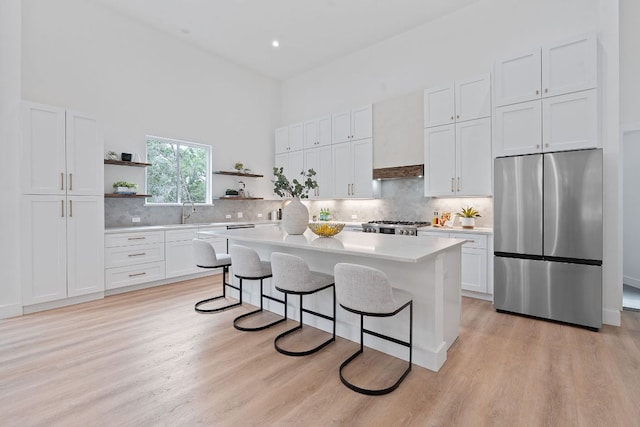 kitchen featuring a center island, open shelves, stainless steel refrigerator, light countertops, and a breakfast bar