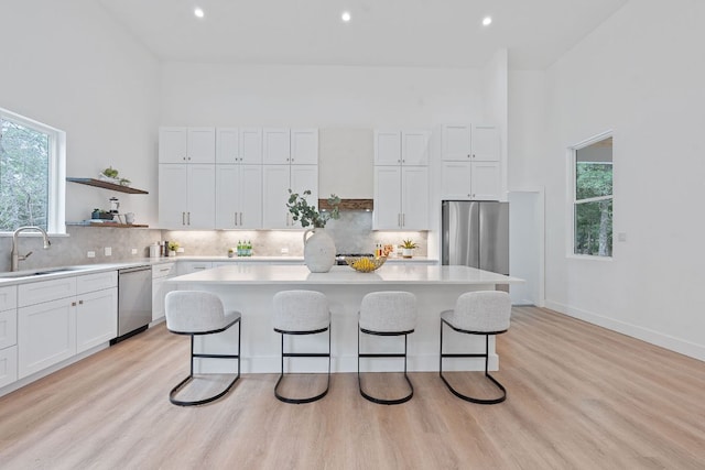 kitchen featuring a kitchen bar, a sink, light countertops, stainless steel appliances, and white cabinetry