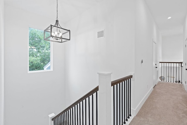 hallway featuring visible vents, an upstairs landing, baseboards, a chandelier, and carpet flooring