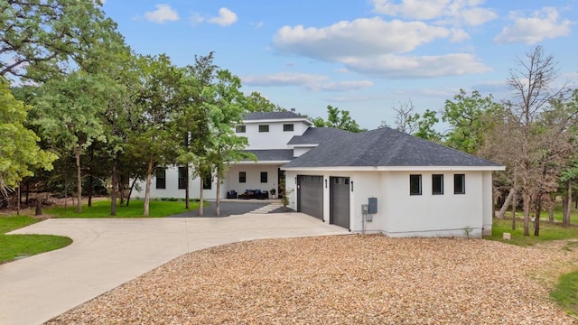 back of property featuring driveway, a lawn, an attached garage, a shingled roof, and stucco siding